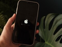 Una mano sostiene un iPhone; en la pantalla se ven iluminados el logotipo de Apple y una barra de progreso.