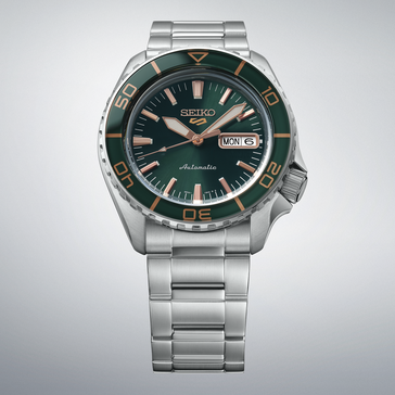 Seiko 5 Sports SKX HDB005 con esfera verde oscuro, bisel verde a juego, agujas e índices de color oro rosa y brazalete de acero inoxidable, mostrado sobre un fondo gris claro.