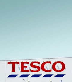Cartelería exterior de Tesco fotografiada contra un cielo despejado (Fuente de la imagen: Simone Hutsch vía Unsplash)