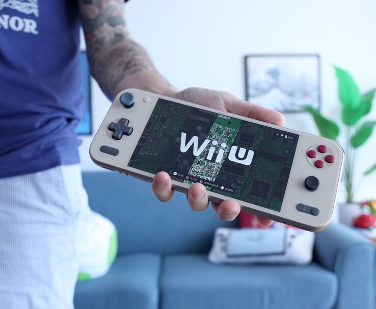 Russ de Retro Game Corps sosteniendo la consola portátil Ayaneo Pocket S2 que ejecuta un emulador de Wii U, con el dispositivo en primer plano en un salón. (Fuente de la imagen: Retro Game Corps)