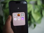 Una mano sostiene un smartphone en el que se ve una carpeta llamada «IA» con aplicaciones como Gemini, ChatGPT y Claude.