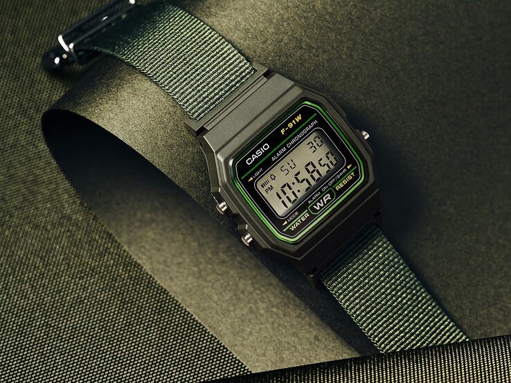 Reloj digital Casio F-91WF-3A con caja negra con detalles en verde y correa de tejido verde, fotografiado sobre un fondo texturizado de color verde oscuro.