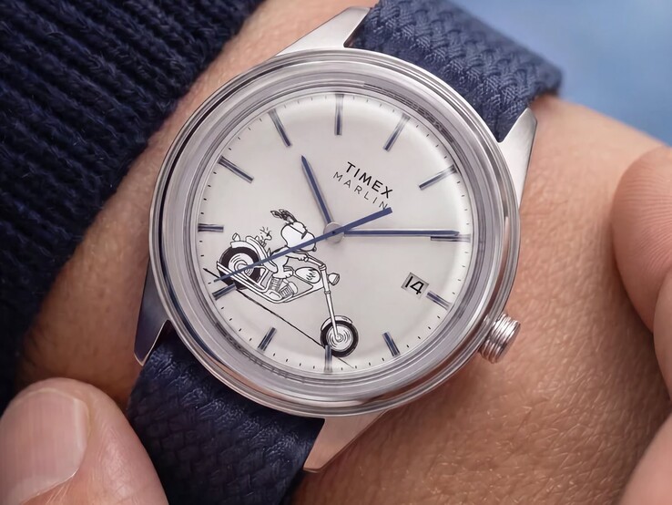 El reloj Peanuts x Timex Marlin Jet Automatic Easy Rider, lucido en la muñeca, muestra a Snoopy montado en una motocicleta en la esfera de color blanco plateado, con índices y agujas azules, y una correa de tejido azul.