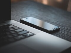 Un smartphone junto a un ordenador portátil abierto sobre un escritorio oscuro