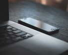 Un smartphone junto a un ordenador portátil abierto sobre un escritorio oscuro