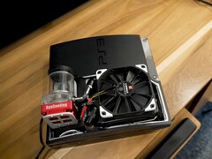 PlayStation 3 personalizada refrigerada por agua con una bomba roja SysCooling y un gran ventilador negro montado en el interior de la carcasa, colocada sobre un escritorio de madera. (Fuente de la imagen: Zac Builds vía YouTube)