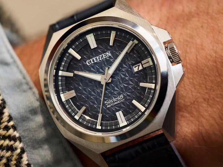 Reloj automático Citizen Serie 8 831 con esfera geométrica en tonos naranja quemado y marrón, caja y bisel en tono dorado, y brazalete integrado de eslabones en forma de H en tono dorado, lucido en una muñeca.