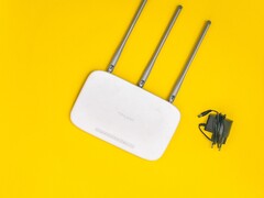 Router Wi-Fi blanco con tres antenas y una fuente de alimentación sobre un fondo amarillo