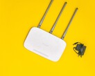 Router Wi-Fi blanco con tres antenas y una fuente de alimentación sobre un fondo amarillo
