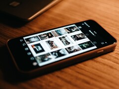 Un smartphone apoyado sobre un escritorio de madera, con la pantalla mostrando una cuadrícula de fotos