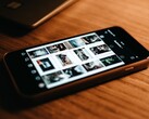 Un smartphone apoyado sobre un escritorio de madera, con la pantalla mostrando una cuadrícula de fotos