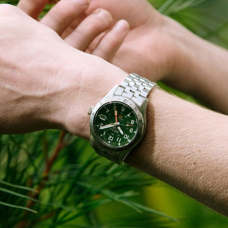 Vista frontal del Seiko 5 Sports Field GMT HDB001, que cuenta con una esfera verde, un bisel fijo de acero inoxidable de 24 horas, un indicador GMT naranja y un brazalete de acero de cinco eslabones.