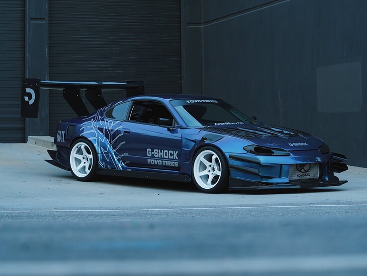 Coche de drift azul con gráficos de G-Shock y Toyo Tires aparcado frente a una nave industrial.