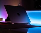 Un MacBook entreabierto en una habitación oscura, con la luz que se cuela por la rendija y se derrama sobre el escritorio