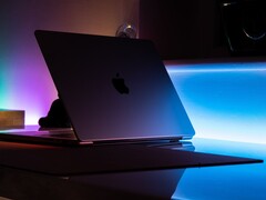 Un MacBook entreabierto en una habitación oscura, con la luz que se cuela por la rendija y se derrama sobre el escritorio
