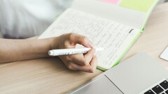 Una persona está tomando notas en un cuaderno junto a un ordenador portátil abierto