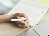 Una persona está tomando notas en un cuaderno junto a un ordenador portátil abierto