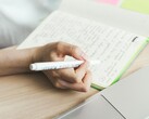 Una persona está tomando notas en un cuaderno junto a un ordenador portátil abierto
