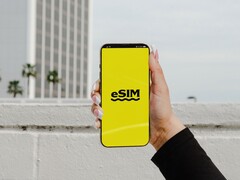 Una mano que sostiene un smartphone con la palabra «eSIM» en letras grandes sobre una pantalla amarilla.