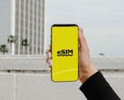 Una mano que sostiene un smartphone con la palabra «eSIM» en letras grandes sobre una pantalla amarilla.
