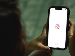 Mujer que sostiene un smartphone con ambas manos; en la pantalla se ve la pantalla de inicio de Instagram