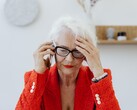 Una mujer mayor, de pelo blanco y con gafas, hablando por teléfono en un salón luminoso, con la mano apoyada en la sien.