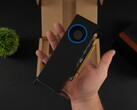 Una persona sostiene la GPU Intel Arc Pro B50 de bajo perfil para estaciones de trabajo con un refrigerador tipo soplador, mostrada contra su caja de embalaje. (Fuente de la imagen: ETA Prime vía YouTube)