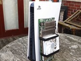 Una consola PlayStation 5 colocada junto a una placa AMD BC250 fabricada a medida y montada con un disipador térmico y un ventilador de refrigeración. (Fuente de la imagen: Budget-Builds Official vía YouTube)