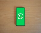 Un smartphone sobre un escritorio de madera en el que se ve la pantalla de inicio verde de WhatsApp con su logotipo.