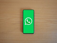 Un smartphone sobre un escritorio de madera en el que se ve la pantalla de inicio verde de WhatsApp con su logotipo.